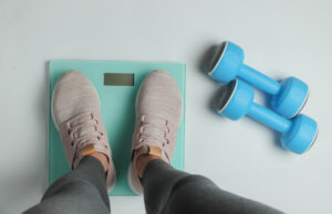 Picture of a person standing on a scale next to dumbbells.