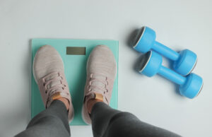 Buy HCG Shots Online Picture of a person standing on a scale next to dumbbells.