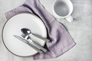 Picture of a cup, plate, knife, fork, spoon, and cloth napkin.