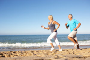 Senior couple in fitness clothing running along a beach