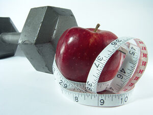 An apple wrapped in a tape measure next to a dumbbell 